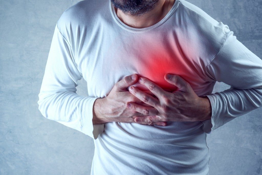Severe heartache, man suffering from chest pain, having heart attack or painful cramps, pressing on chest with painful expression.