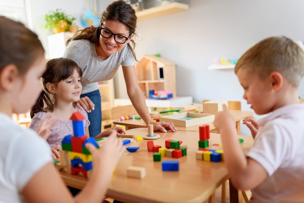 children and teacher in preschool classroom playing blocks
