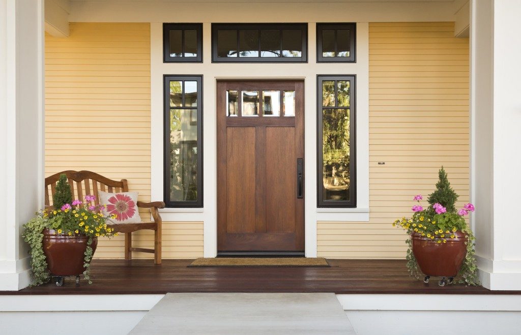 Front view of a wooden front door on a yellow house with reflections in the window and a wide view of the porch and front walkway