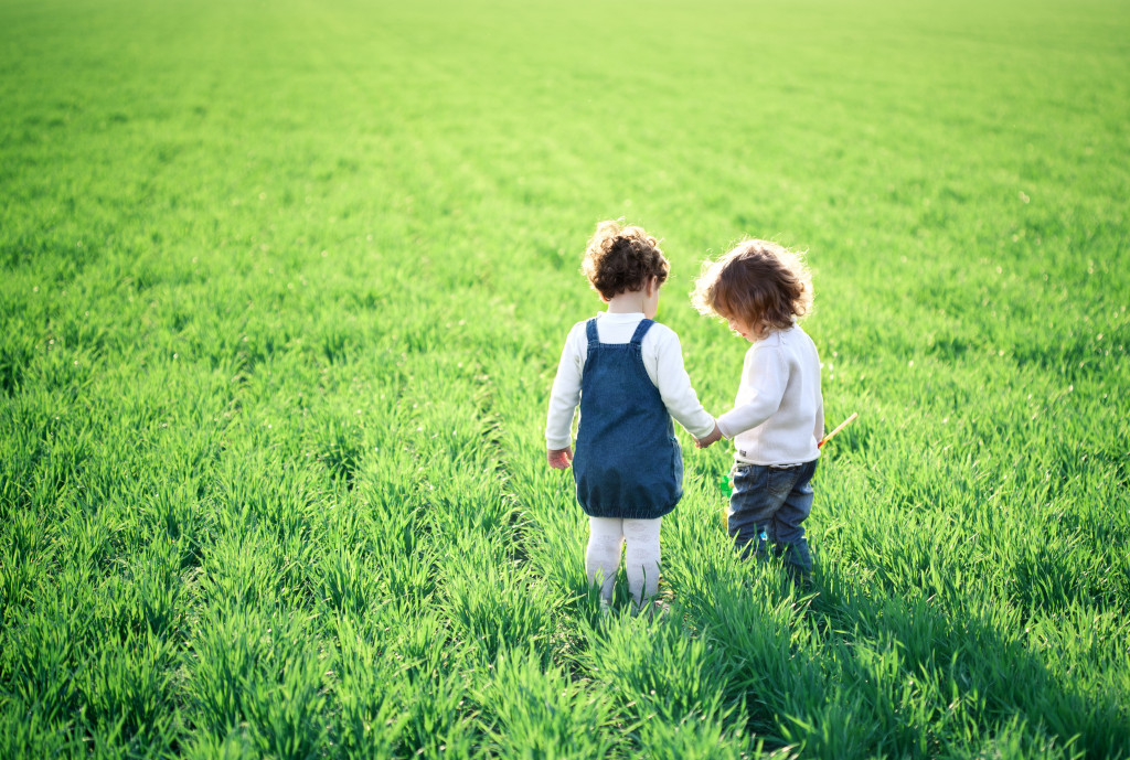 two young kids holding each other's hand in a field of grass