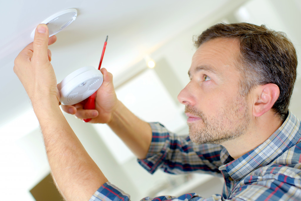 a man placing a smoke detector on the ceiling
