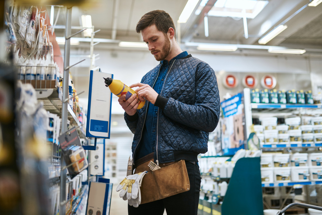 a male DIYer with gloves in his belt bag and looking at some fluid inside a hardware store