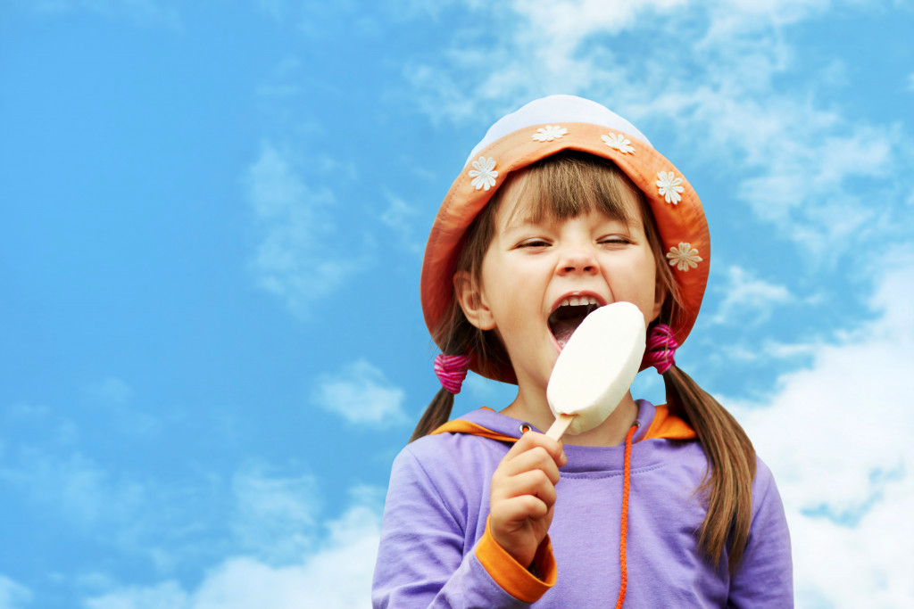 A young girl eating an ice cream on a popsicle stick with a sky background
