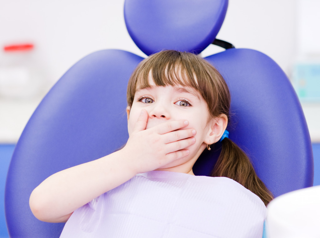 child covering her mouth using her hand in a dentist chair