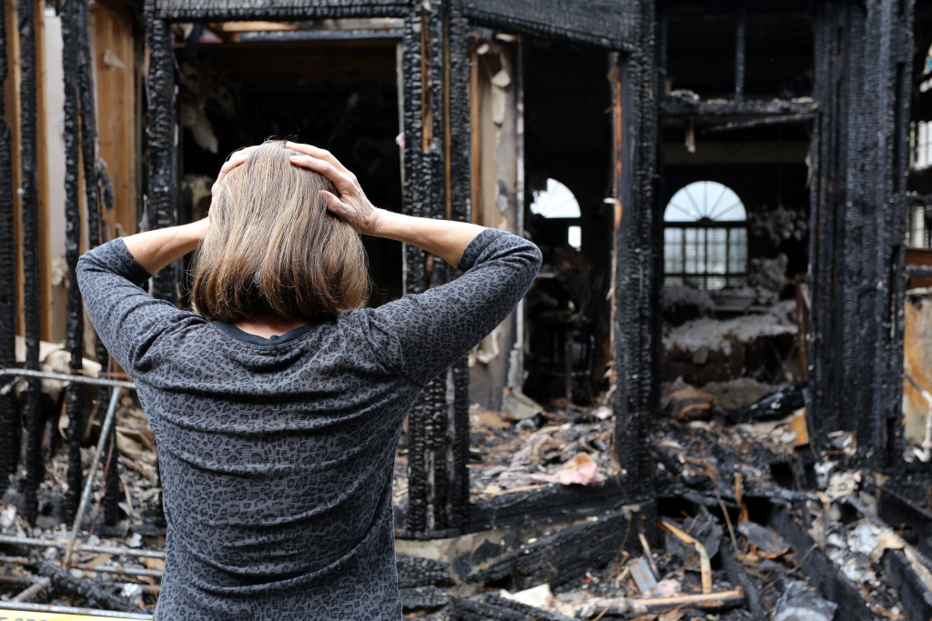 a shocked and grieving woman because of a house that is devoured by fire