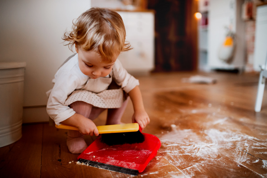 A small kid sweeping the floor with flour or powder