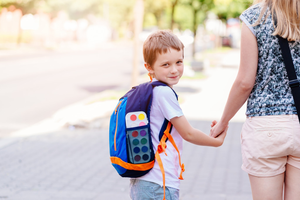 a young boy wearing a backpack holding mom's hand