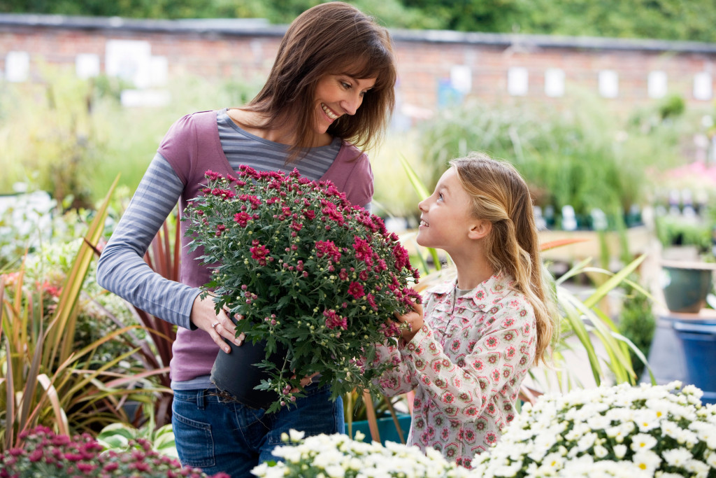 young daughter smiling with mother holding plants in a garden
