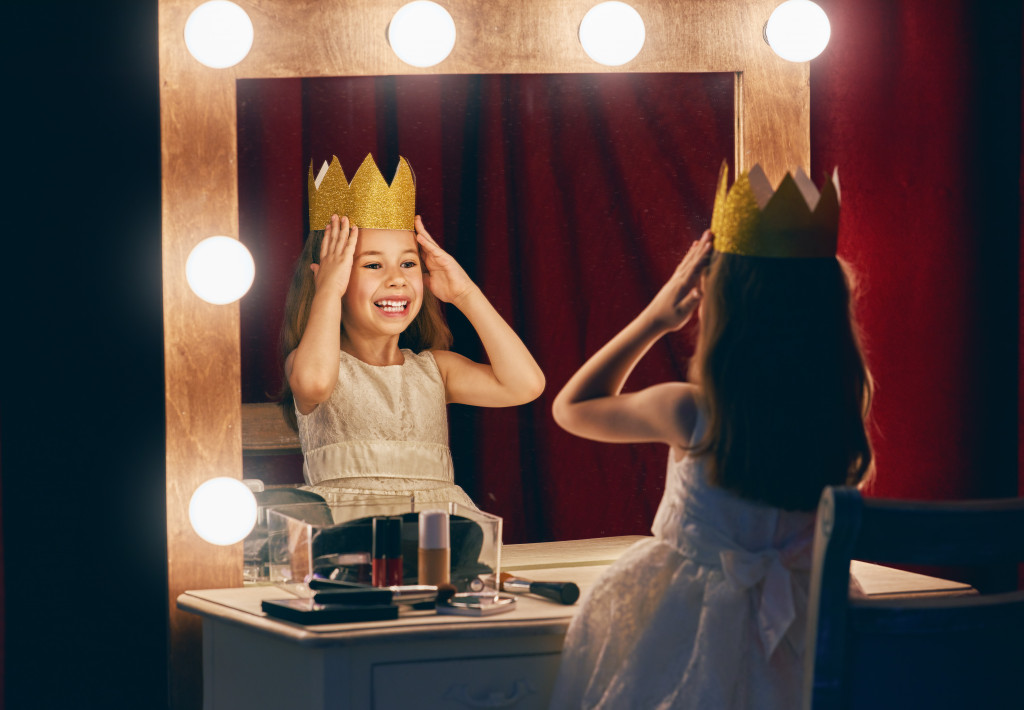 little girl wearing a crown while in front of vanity mirror