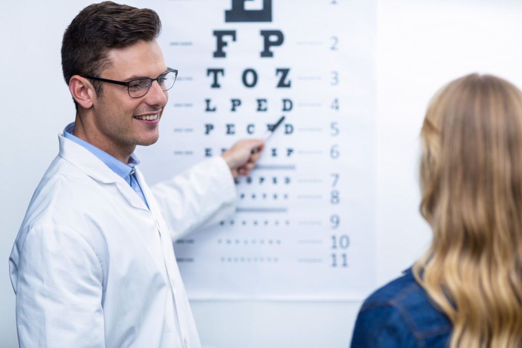 smiling male optometrist assessing a woman's eyesight using a chart