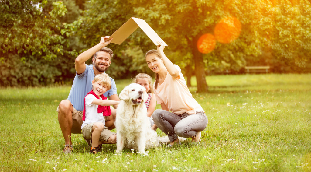 A family with a dog holding up a cardboard as roof outdoors