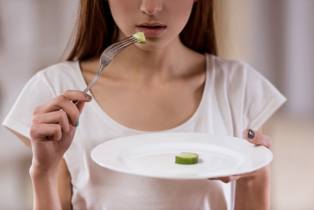 A young girl eating only a slice of cucumber from a large empty plate