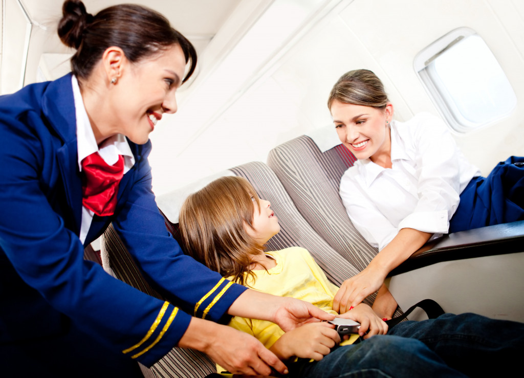 Air hostess helping a child fasten the seatbelt in a plane.