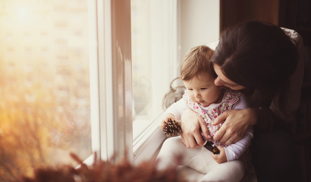 woman holding her child beside the window to catch some sunlight
