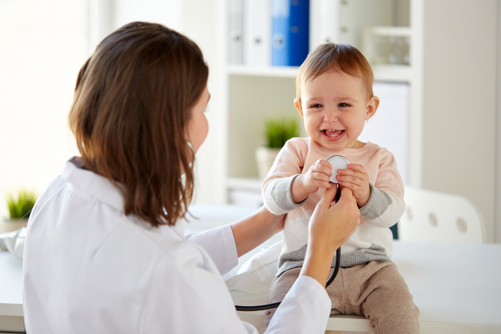 female doctor putting stethoscope at happy laughing child