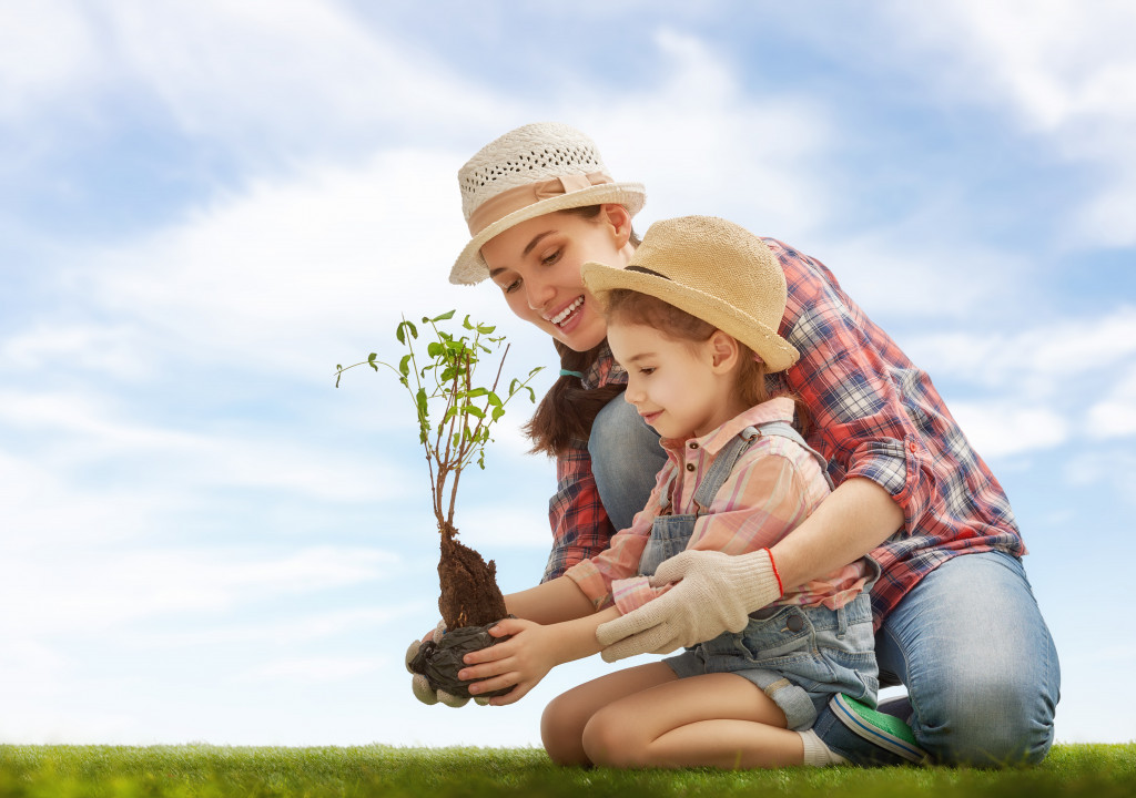 mother and daughter wearing hats while planting a plant in the outdoors