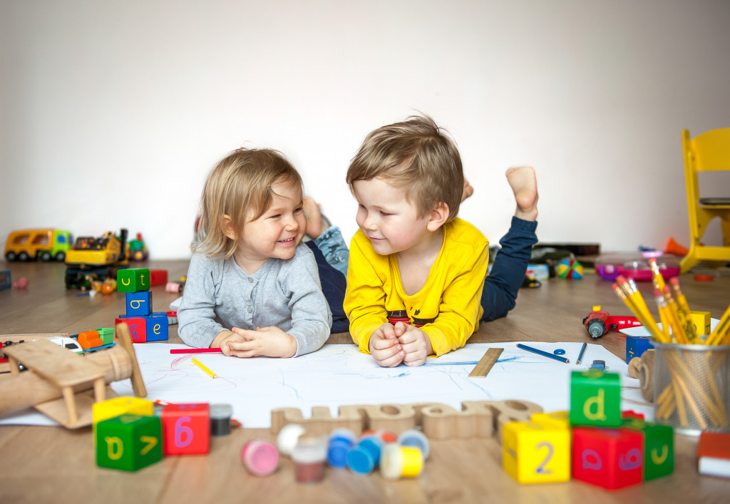 Two young children drawing in a messy playroom