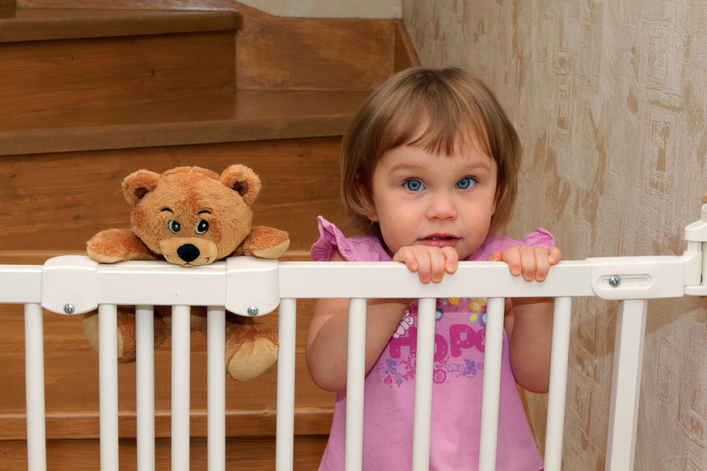 A young girl and her teddy bear behind a gate to the stairs