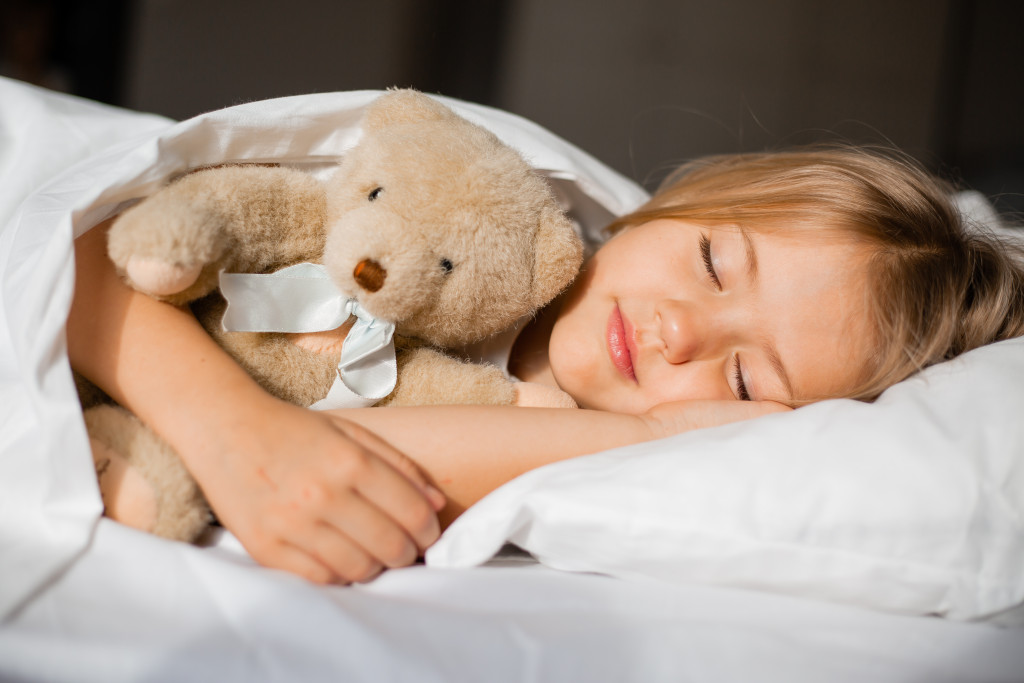 little girl holding teddy bear while tucked in bed sleeping