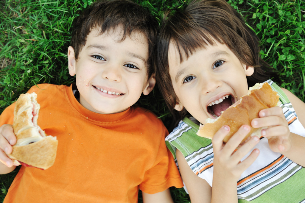 young boy and girl laying down in the grass eating healthy sandwiches