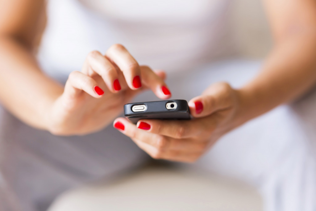 A woman with red nail polish typing on a smartphone