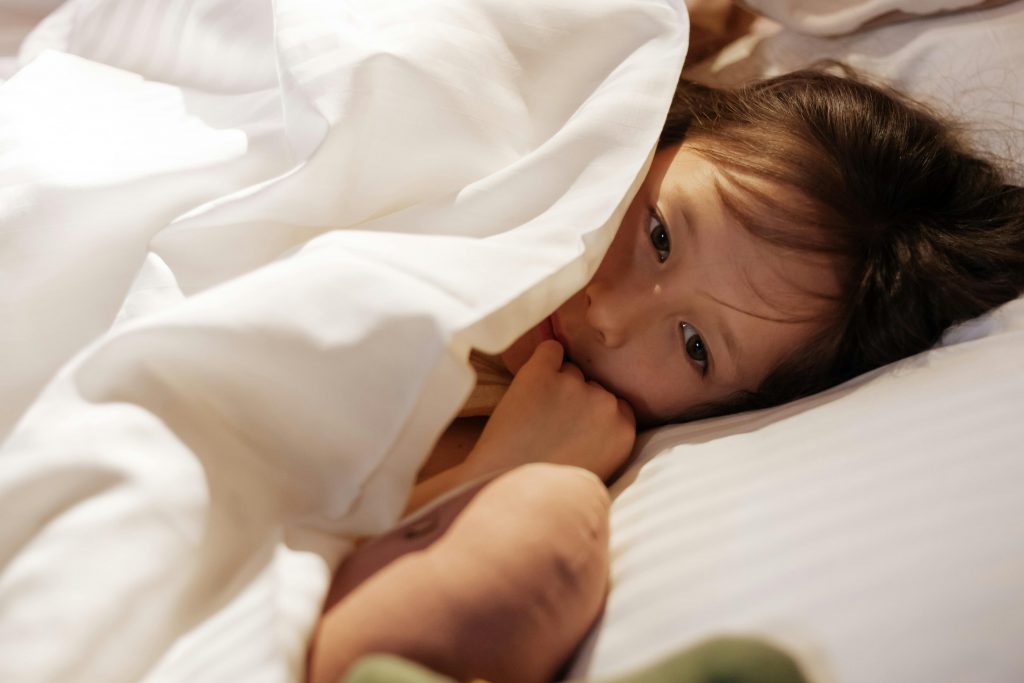 toddler wrapped in a blanket in bed, biting her pinky